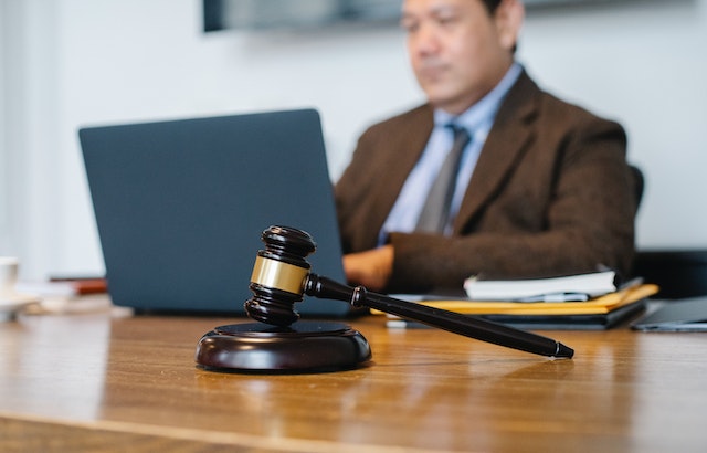 person in suit typing on laptop with gavel in the foreground
