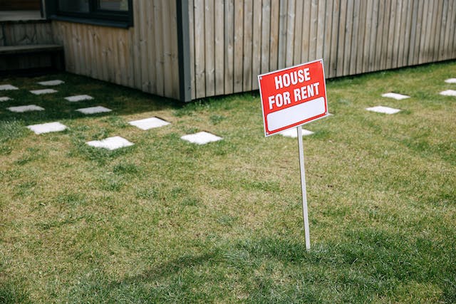 A sign in a front lawn that reads “House for rent”