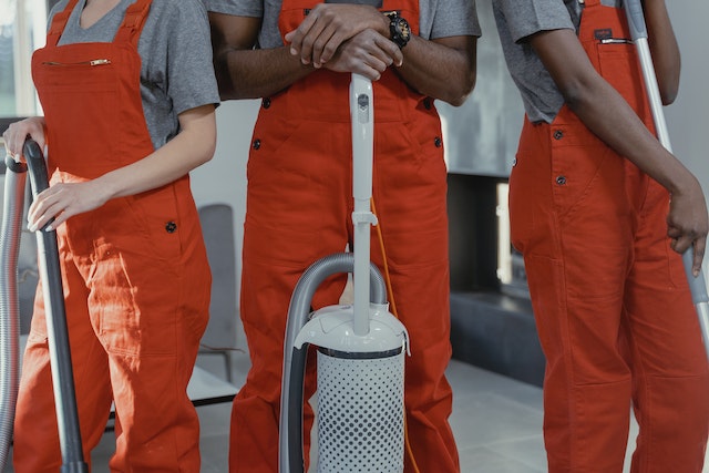 three people in orange overalls with a vacuum